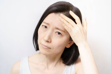 Orta yaşlı bir kadın yüzüne dokunuyor ve cilt sorunları yaşıyor. 