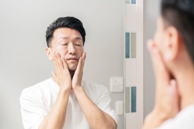 Aynaya bakıp derisinin durumunu kontrol eden bir adam.