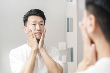 Aynaya bakıp derisinin durumunu kontrol eden bir adam.
