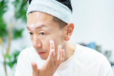 Erkekler odada yüzlerine nemlendirici krem sürüyor.