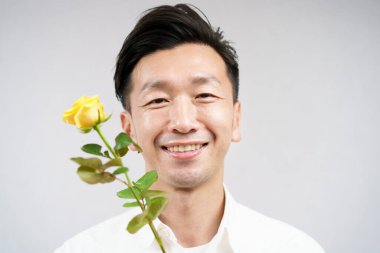 Sarı gül çiçeğiyle gülümseyen Asyalı adam.