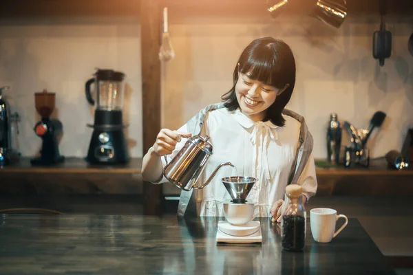 A young woman brewing coffee with a hand drip in a calmly lit space