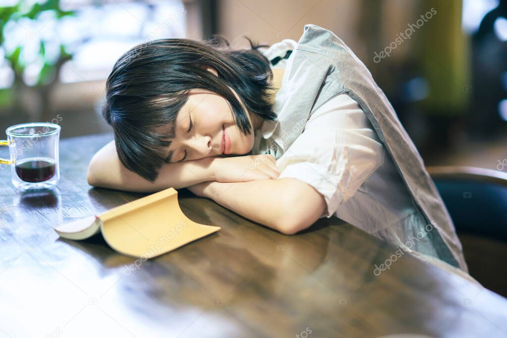 A young woman napping in a moderately bright room with abook and glass of coffee