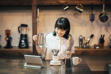 Genç bir kadın, sakin bir şekilde aydınlatılmış bir yerde, elini damlatarak kahve yapıyor.