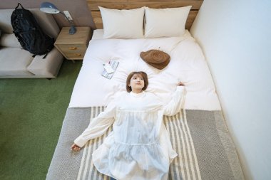 Asyalı bir kadın otel odasında dinleniyor.