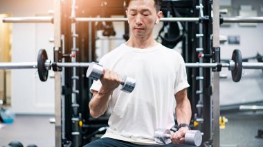 Kilolu bir adam dambıllarla kas çalışması yapıyor.