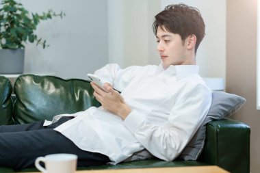 Kanepede dinlenirken akıllı telefon kullanan Asyalı bir adam.