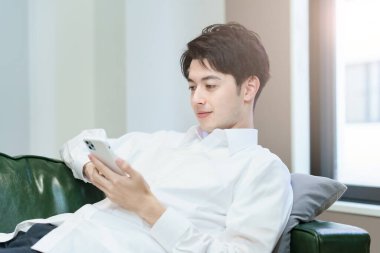 Kanepede dinlenirken akıllı telefon kullanan Asyalı bir adam.