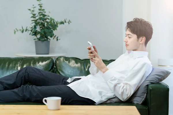 Uomo Asiatico Che Gestisce Uno Smartphone Mentre Rilassa Sul Divano — Foto Stock