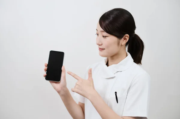 スマートフォンを操作する白いコートのアジアの女性 — ストック写真