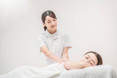 Asyalı genç güzellik uzmanı bir kadına masaj yapıyor.