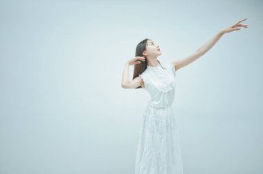 Asyalı genç kadın zarif ve beyaz arka planda dans ediyor.