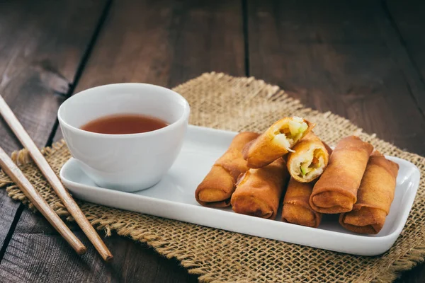 Mini spring rolls with sweet spicy dip and chopsticks on a rustic wooden table