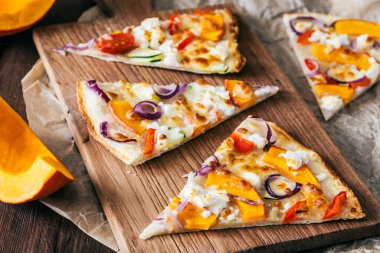 Tahtada balkabaklı tarte flambee, kırmızı soğan ve peynir parçaları.