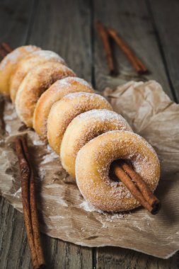 Şekerli mini çörekler ahşap bir masanın üzerindeki tarçın çubuğuna dizilmiş, dikey