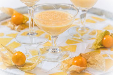 Yuvarlak tepside eggnog ve physalis meyveleriyle dolu bir bardak. 