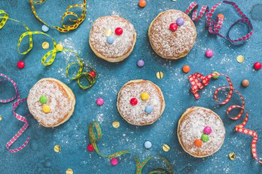 Krapfen, Berliner veya flamalı çörekler, konfeti ve mavi arka planda çikolata çekirdeği. Renkli karnaval ya da doğum günü resmi, üst görünüm.