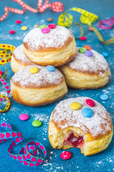 Krapfen, Berliner veya flamalı donut, konfeti ve çikolatalı fasulye. Mavi arkaplanda renkli karnaval veya doğum günü resmi, dikey.