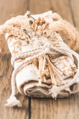 Kurumuş çiçekler ve kurdeleyle süslenmiş rulo peçete veya çay havlusu, ahşap bir masada doğal renklerle süslenmiş masa süsü, çiçeklere odaklı dikey fotoğraf.