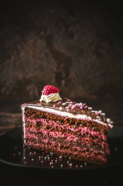 Koyu kahverengi arka planda siyah bir plaka üzerinde ahududulu çikolatalı turta. Kopya alanı ile dikey.