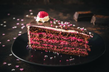Bir parça ahududu çikolatalı turta, koyu kahverengi arka planda siyah bir tabakta.