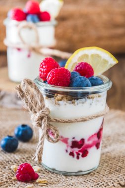 Çilekli yoğurt ve mısır gevreği kırsal bir tahta masada, dikey bir bardakta.