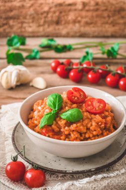 Ev yapımı domatesli risotto. Köy ahşap bir masada taze fesleğen, dikey.