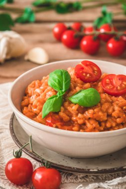 Ev yapımı domatesli risotto. Köy ahşap bir masada taze fesleğen, dikey.