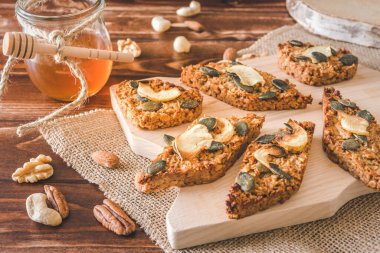 Ev yapımı elma taneli gofretler, kurutulmuş elma ve balkabağı tohumlarıyla süslenmiş, ahşap arka planda bir ahşap slat üzerine uzanmış.