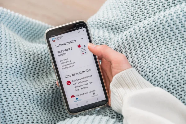 Almanya - 27 Mart 2021: Resmi Alman Corona Uyarı Uygulaması, kadın bir el tarafından tutulan akıllı telefondan olumlu bir Covid-19 test sonucuyla sonuçlandı. Çeviri: befund positiv: sonuç pozitif, Bitte beachten Sie: Lütfen not edin.