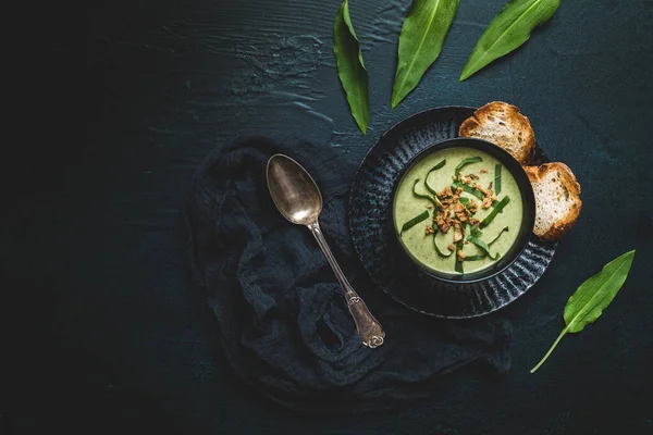 Wild garlic soup with wild garlic leaves and rosted onions on black background, top view with copy space