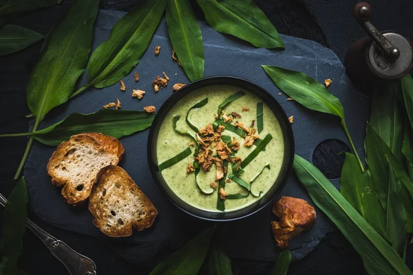 Wild garlic soup with wild garlic leaves and rosted onions on black background, top view