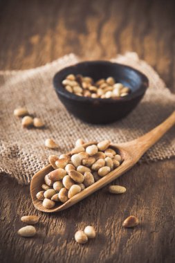 Tahta kaşıkta çam fıstığı ve tahta arka planda küçük bir kase, dikey.