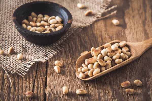 Ahşap bir kaşıkta çam fıstığı ve tahta bir arka planda küçük bir kasede