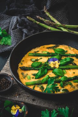 Yeşil kuşkonmazlı omlet, siyah arka planda fesleğen ve otlar, dikey