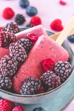 Ev yapımı meyveli yoğurt, pembe arka planda bir kasede buzlu dondurma, dikey yakın plan.