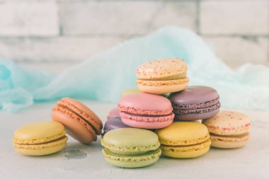 Beyaz bir duvarın önüne istiflenmiş pastel renkli Fransız kurabiyeleri.