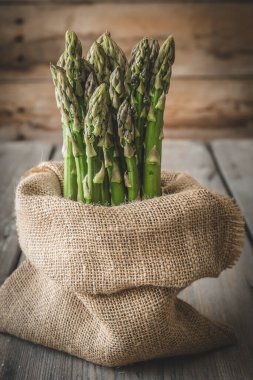 Bir çuval dolusu yeşil kuşkonmaz tahta bir masanın üzerinde dikey duruyor.