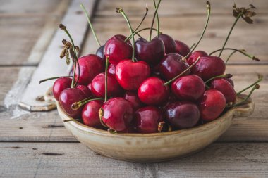 Köhne ahşap bir masada taze kırmızı kirazlı köy kasesi.