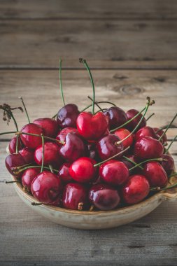 Köy ahşap bir masa üzerinde taze kırmızı kirazlarla dolu kırsal bir kase. Kopya alanı ile dikey.