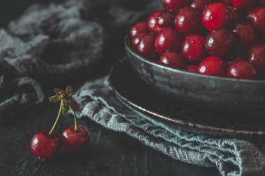 Siyah arka planda siyah bir kasede olgun kirazlar.