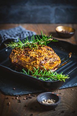 Tek parça biftek, hardal-bitki kabuğuyla servis edilmiş, fırından yeni çıkmış, ahşap bir masada, dikey.