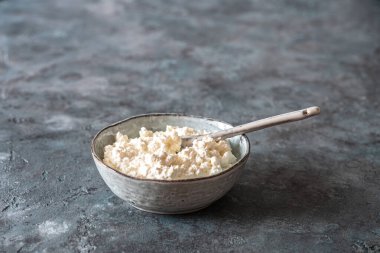 Gri arka planda süzme peynirli gri kase. Süzme peynir peynir peynir yapma işlemi sırasında taze pastörize sütten yapılır. Boşluğu kopyala.