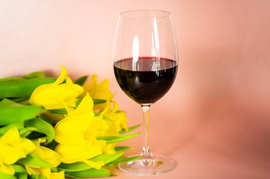 Masada laleler olan şarap kadehi, pembe arka plan.