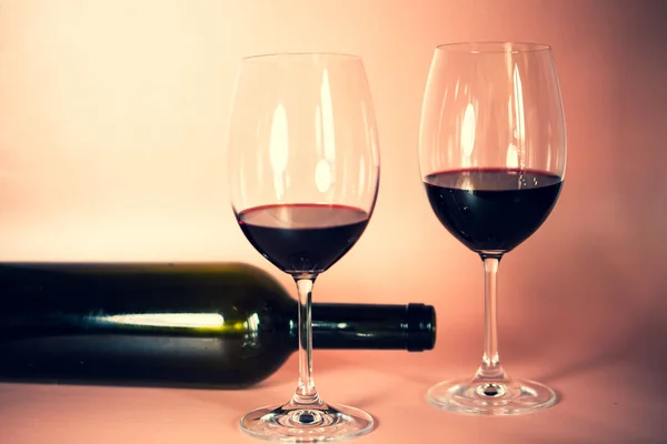 two wine glasses with wine bottle, pink background