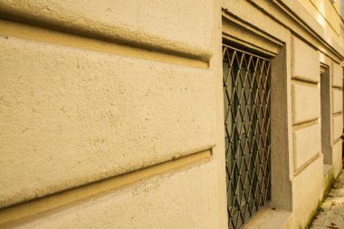 Önünde parmaklıklar olan eski bodrum penceresi, yeşil pencere, bej ev cephesi.