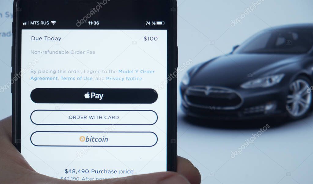 Buying Tesla with Bitcoin. Smartphone paying for Tesla car with BTC. Moscow 24 March 2021.