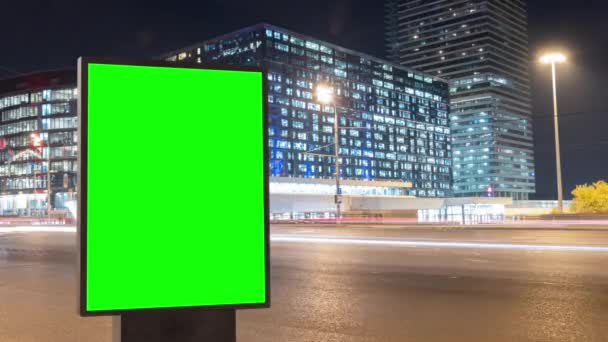 Современный рекламный щит с зеленым экраном для рекламы на оживленном шоссе с дорожным движением и небоскребами, время движения ночью — стоковое видео