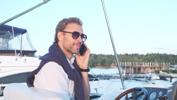 Przystojny, odnoszący sukcesy facet na jachcie rozmawiający przez telefon komórkowy. Portret biznesmena na żaglówce o zachodzie słońca. — Wideo stockowe
