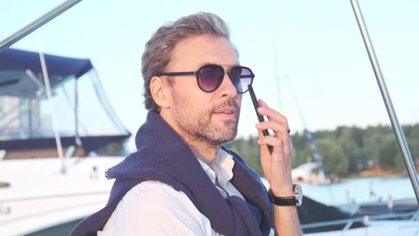 Hezký úspěšný muž na jachtě mluví na mobilu. Portrét obchodníka na plachetnici při západu slunce. — Stock video